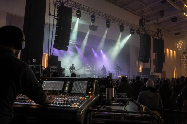 Live sound mixing console, line-array speakers and violet stage lighting